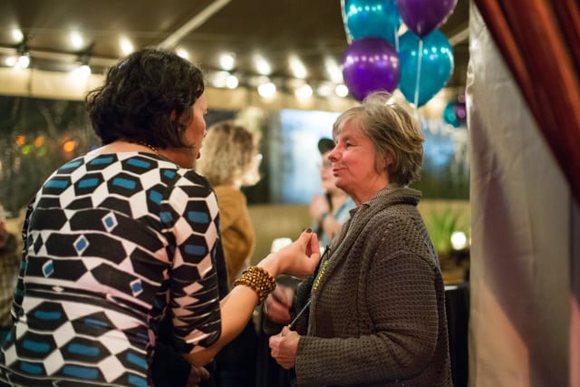 Women engaging in conversation at Love Bomb 2017 event, with festive decorations and balloons in the background, highlighting community engagement and support for My Voice Music nonprofit.